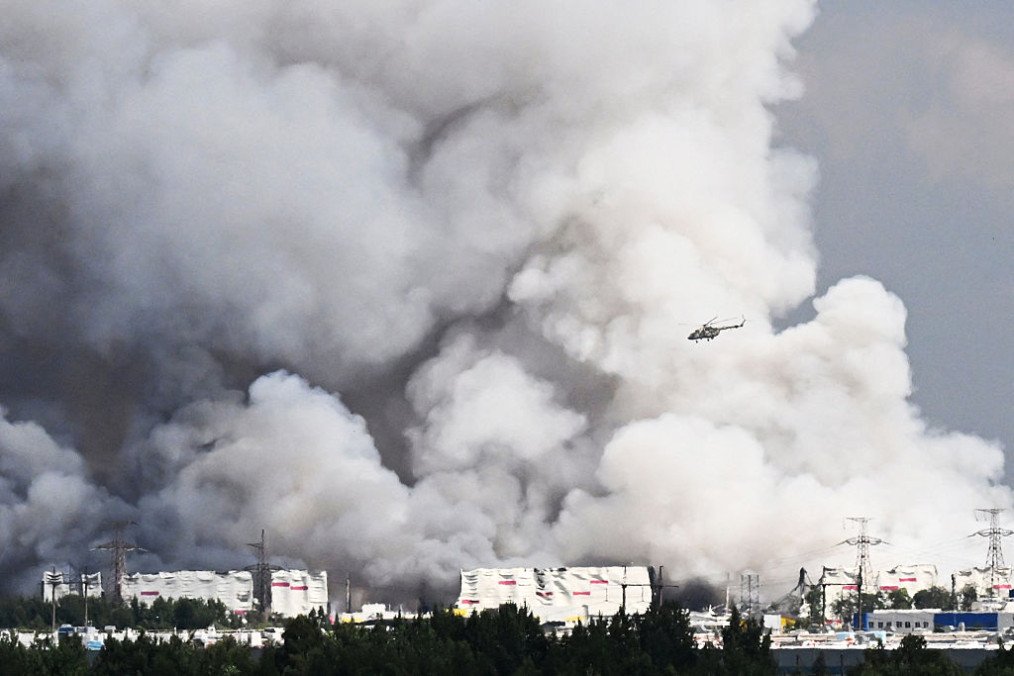 A helicopter flies past smoke rising from a warehouse for a Russian e-commerce giant near Saint Petersburg after being hit by Ukrainian drones early on July 24, 2026. (Source: Getty Images)