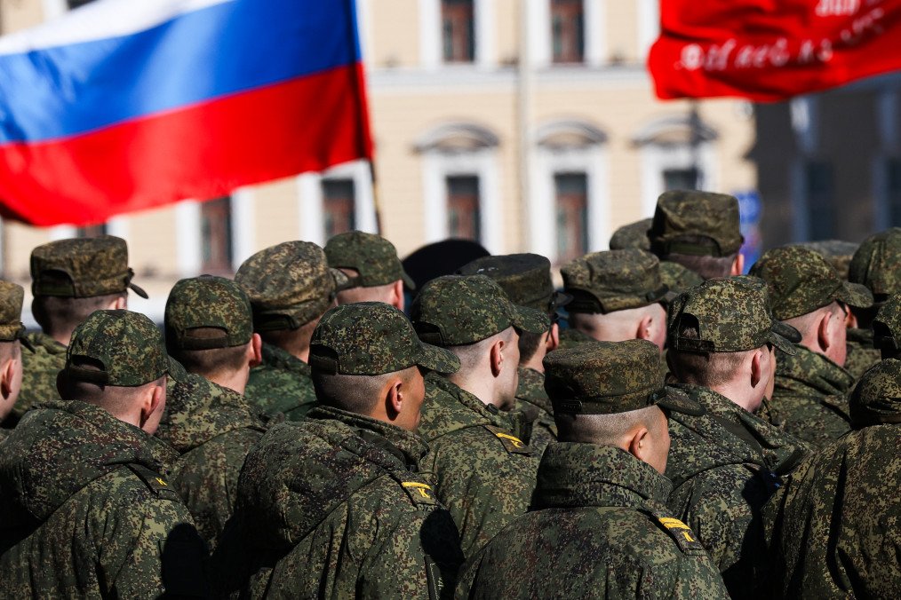 Military personnel in camouflage uniforms and field caps standing in formation under the National Flag of Russia. (Source: Getty Images)