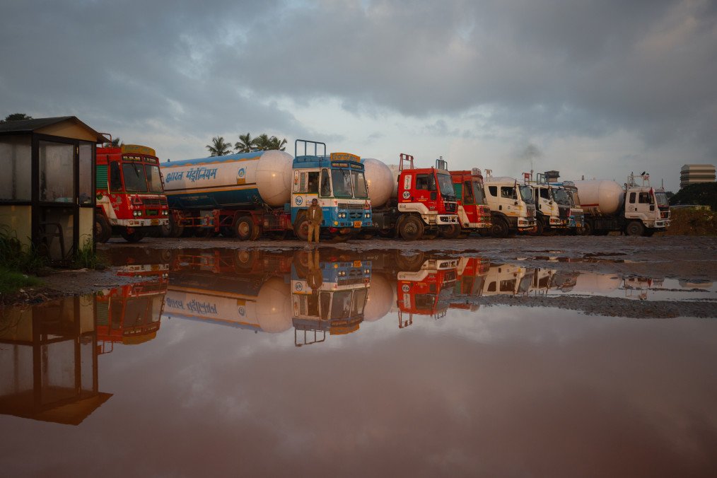 A truck driver and parked trucks are reflected in a puddle outside the Mangalore Refinery and Petrochemicals Limited (MRPL) parking terminal on September 05, 2025, in Mangaluru, India