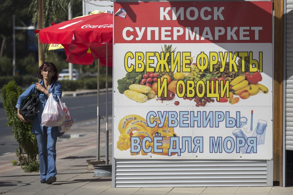 A pedestrian carries grocery bags past a supermarket advertisement written in Russian cyrillic script in Limassol, Cyprus, on April 8, 2014. Illustrative photo. (Source: Getty Images)