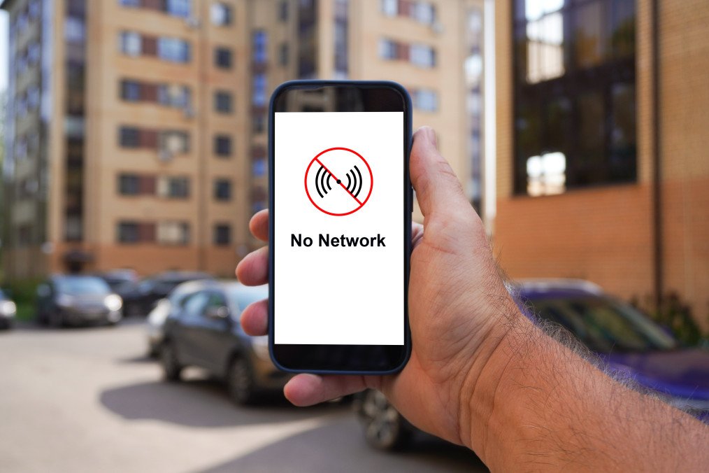Man holding a smartphone displaying a “No Network” message in a residential area. (Source: Getty Images)