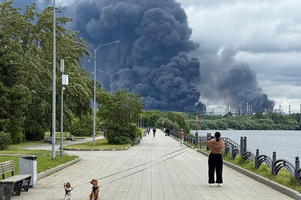 People walk in a park as black smoke rises from the area of the Russian oil producer Gazprom Neft’s Moscow oil refinery on the south-eastern outskirts of Moscow on June 18, 2026. (Source: Getty Images)