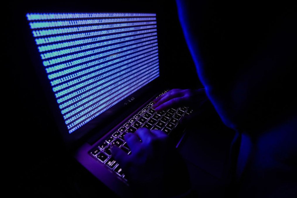 A person dressed as an internet hacker is seen with binary code displayed on a laptop screen, illustrative image. (Source: Getty Images)