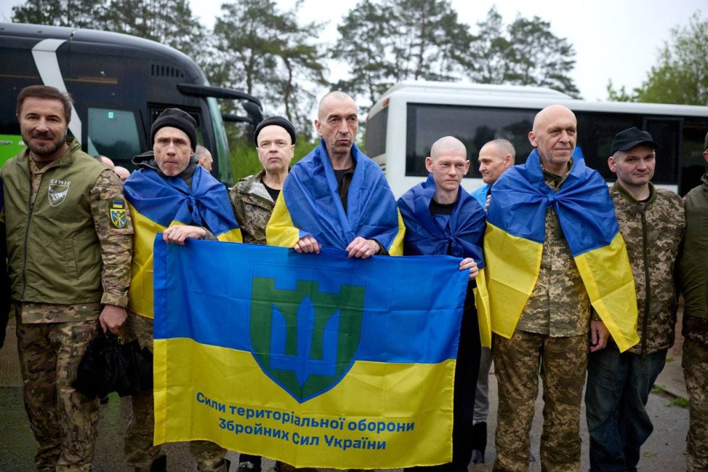 Un grupo de soldados ucranianos liberados desciende de un autobús en la zona de intercambio; algunos visten ropa deportiva y otros uniformes, mostrando expresiones de alivio al volver a territorio controlado.