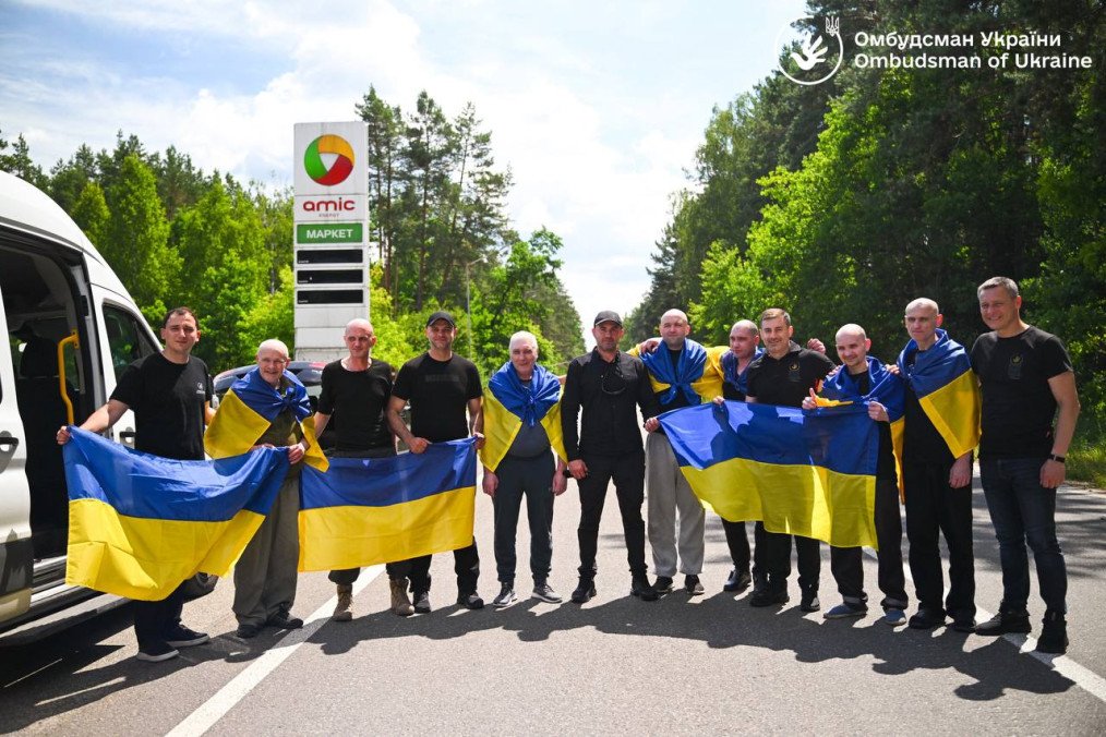 Seven Ukrainian civilians returned from Russian captivity pose with national flags after arriving in Ukraine on June 27, 2026. (Source: Office of the Ukrainian Parliament Commissioner for Human Rights)