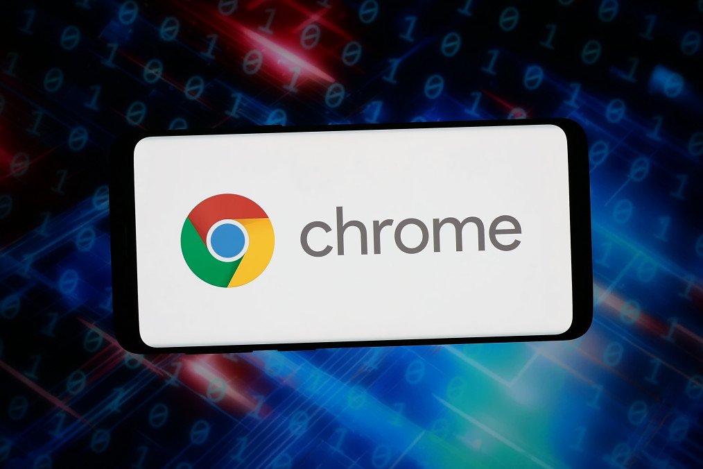 The logo of web browser Google Chrome is displayed on a smartphone in front of abstract background on computer screen. (Source: Getty Images)