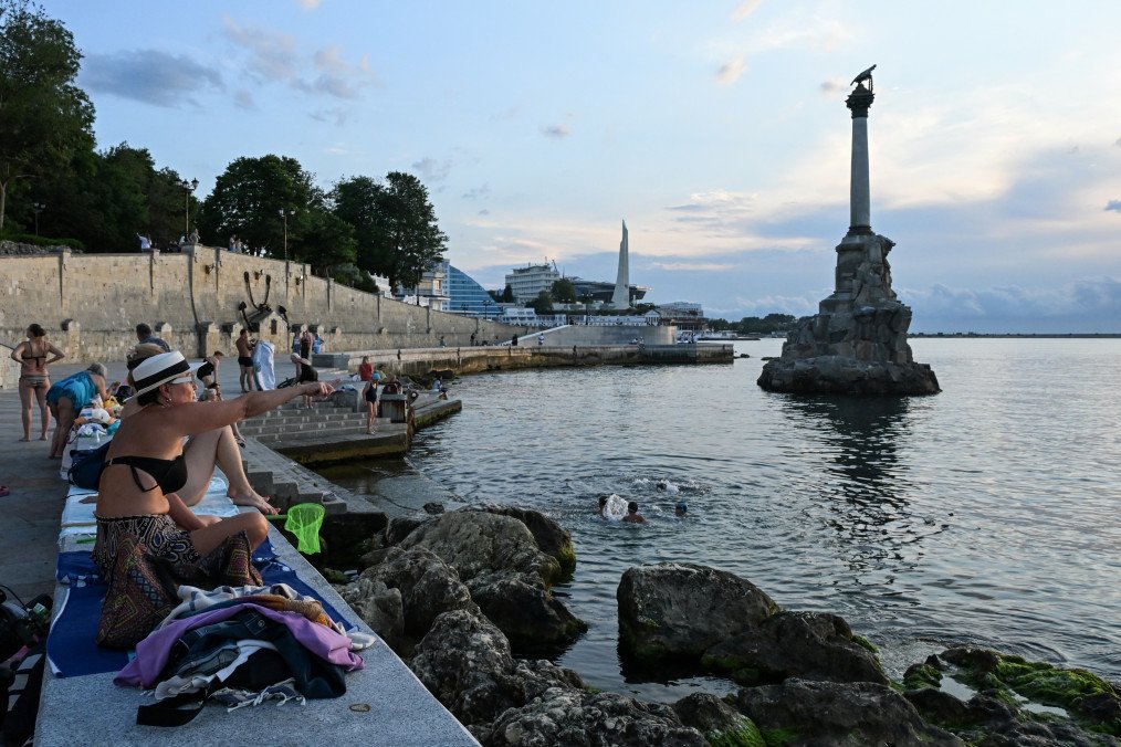 People sit on an embankment with the Monument of The Sunken Ships in the background in central Sevastopol. (Source: Getty Images)