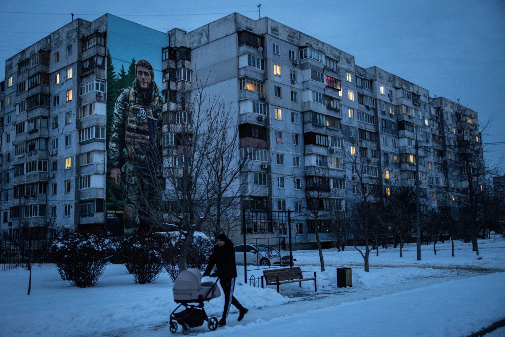 A man walks past a building suffering from limited electricity and painted with the mural of a fallen Ukrainian soldier on February 18, 2026 in Kyiv, Ukraine. (Source: Getty Images)