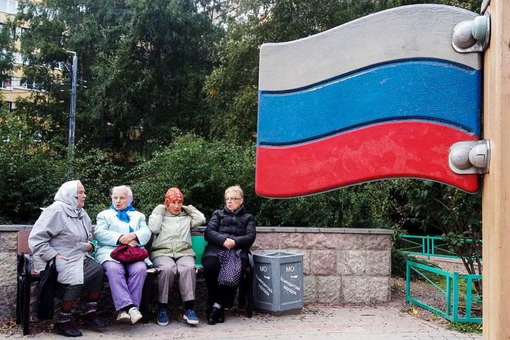 A group of elderly women sit on a bench next to a wooden Russian national flag. (Source: Getty Images)