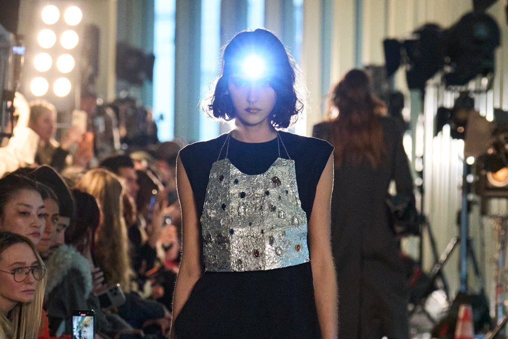 A model confidently walks the runway in a unique metallic embellished top paired with relaxed black pants and knee-high boots, accented by a headlamp. (Source: LITKOVSKA press office)