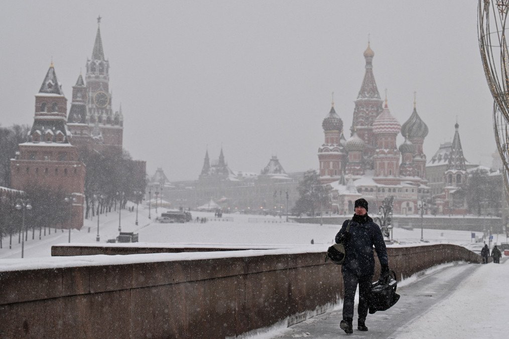 A man walks along a bridge over the Moskva River in central Moscow, with the Kremlin’s Spasskaya Tower and St. Basil’s Cathedral visible in the background on a snowy day, February 12, 2026. (Source: Getty Images)
