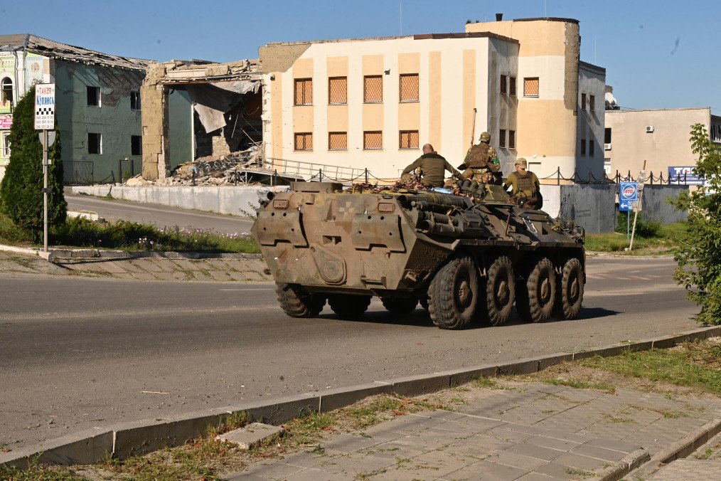 Ukrainian servicemen ride atop an armored personnel carrier (APC) past a destroyed building in the town of Kupiansk, Kharkiv region, on August 17, 2023. (Source: Getty Images)