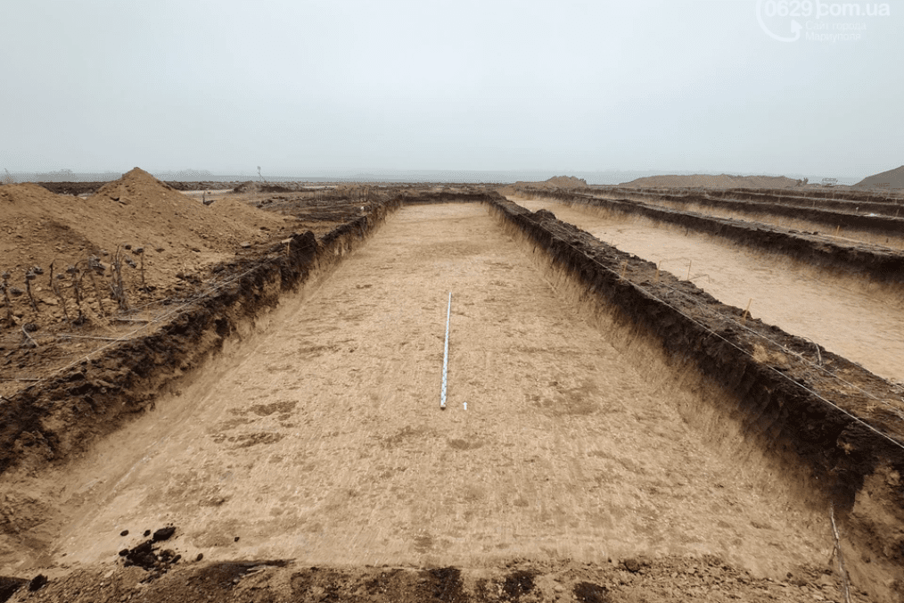 A large excavation site with deep rectangular trenches carved into the earth, prepared ground leveled and measured amid an overcast landscape. (Source: Mariupol website)