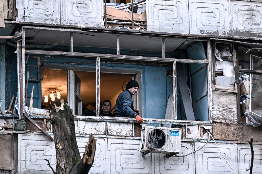 People stand on a balcony of a residential multi-storey building damaged as a result of a Russian strike drone hit in Zaporizhzhia, Ukraine, on February 26, 2026. (Source: Getty Images)