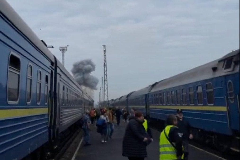 Passengers stand between trains as smoke rises near a railway station following a Russian attack. (Source: Pivden)