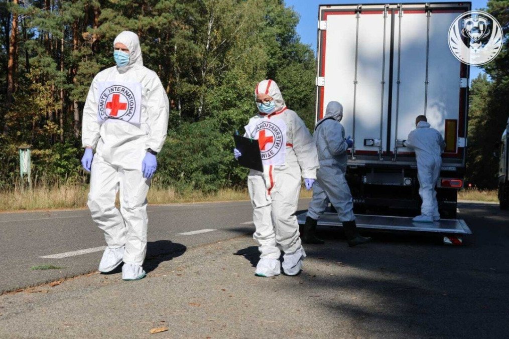 ICRC personnel in protective suits supervise the transfer of repatriated bodies from refrigerated trucks. (Source: Coordination HQ for the Treatment of POWs)