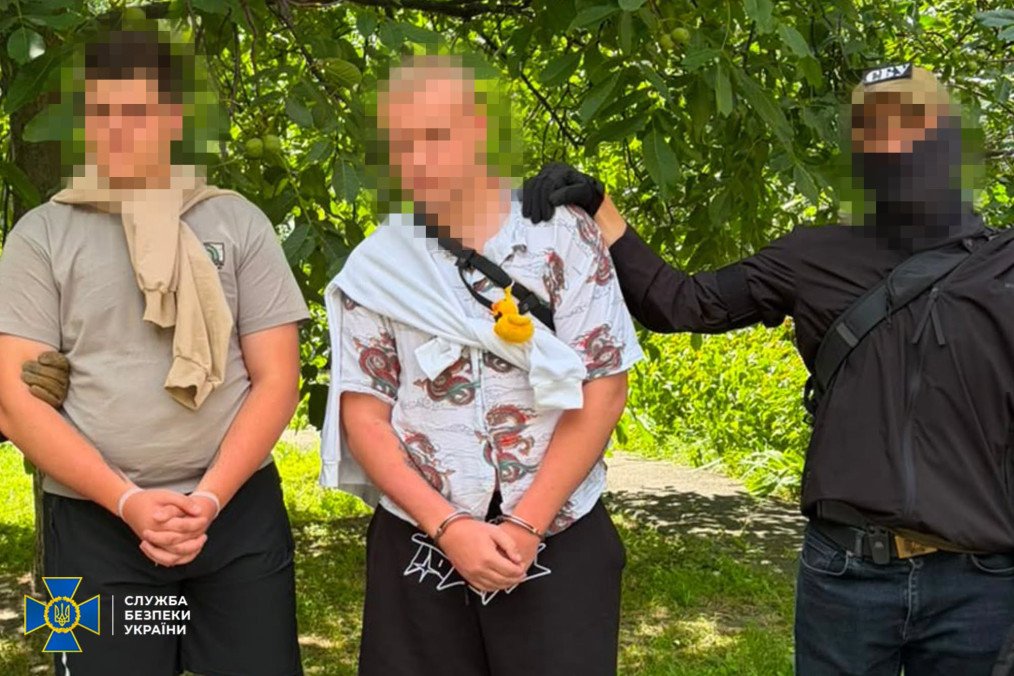 Two handcuffed men stand beside a masked Security Service of Ukraine officer after being detained in Kyiv for registering Starlink terminals for the FSB. (Source: SBU) Two handcuffed men stand beside a masked Security Service of Ukraine officer after being detained in Kyiv for registering Starlink terminals for the FSB. (Source: SBU)