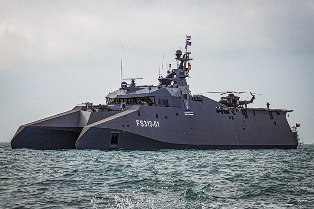 The dark-grey, stealth-designed Iranian catamaran warship Soleimani sails on open water, carrying a helicopter on its rear deck. (Source: Tasnim News Agency)