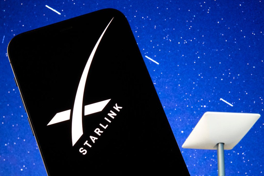 The SpaceX Starlink logo is seen displayed on a smartphone screen, with a Starlink satellite dish visible in the background. Illustrative Image. (Source: Getty Images) The SpaceX Starlink logo is seen displayed on a smartphone screen, with a Starlink satellite dish visible in the background. Illustrative Image. (Source: Getty Images)