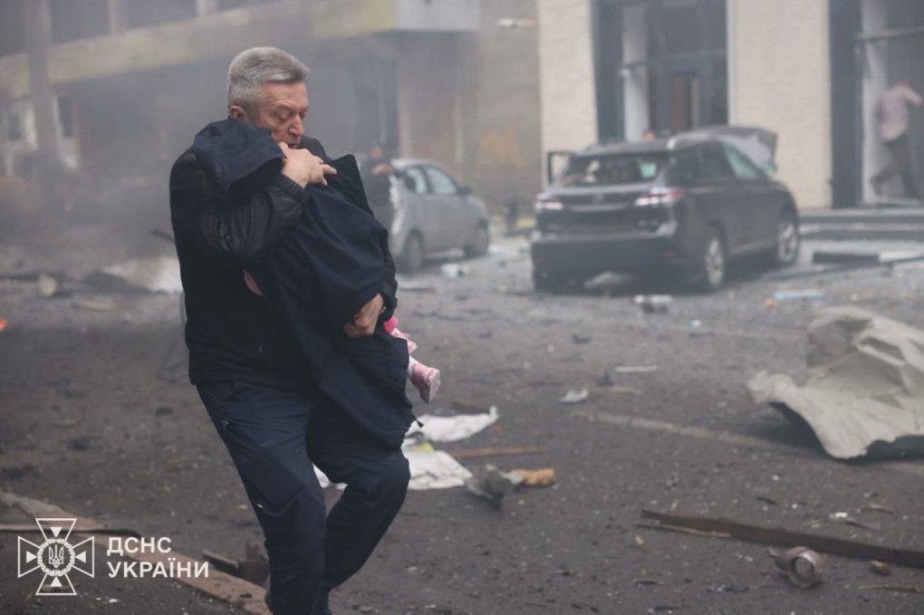 A man shields a child while evacuating through smoke-filled streets after the Russian drone strike on the Kharkiv kindergarten. (Source: Ukrainian President Volodymyr Zelenskyy)