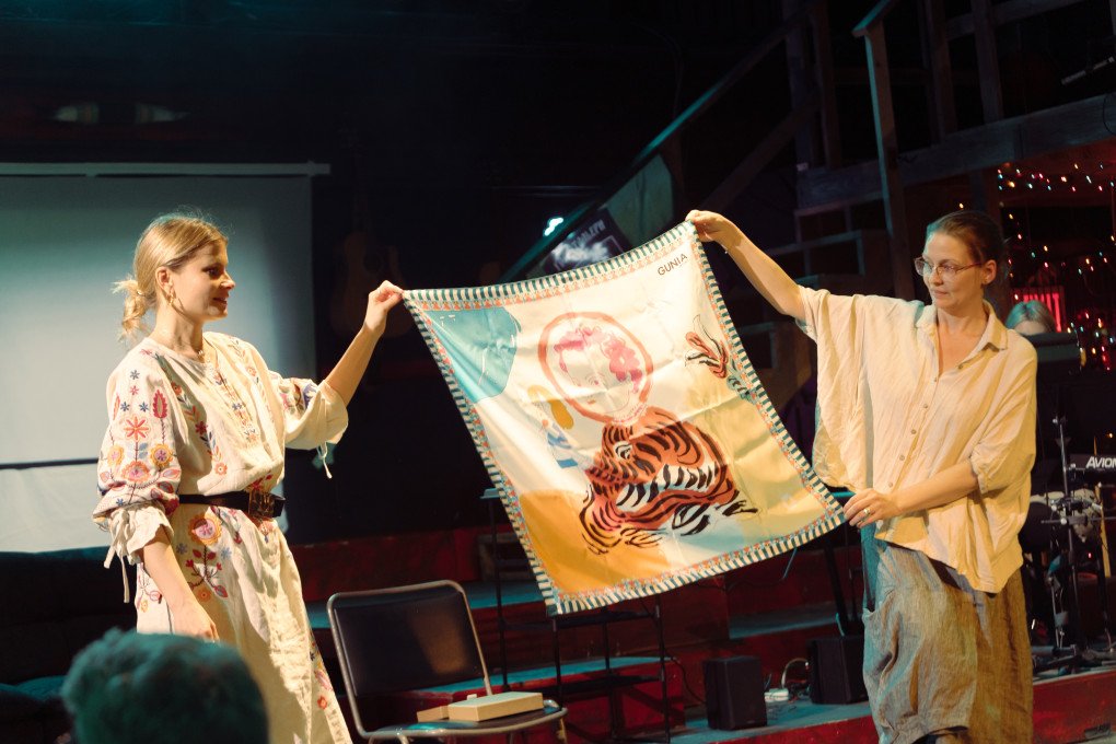 Daria Kolomiec and Musa Gurnis holding a silk scarf—one of the auction items presented during the February 24, 2025 “Diary of War” theater reading. Photo: Tania Nikolaienko Daria Kolomiec and Musa Gurnis holding a silk scarf—one of the auction items presented during the February 24, 2025 “Diary of War” theater reading. Photo: Tania Nikolaienko