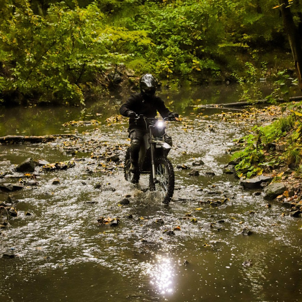 A rider in tactical gear crosses a shallow stream on a WolfStorm electric motorcycle, demonstrating the vehicle’s off-road and all-weather capabilities. (Source: UkrSpecConsulting)