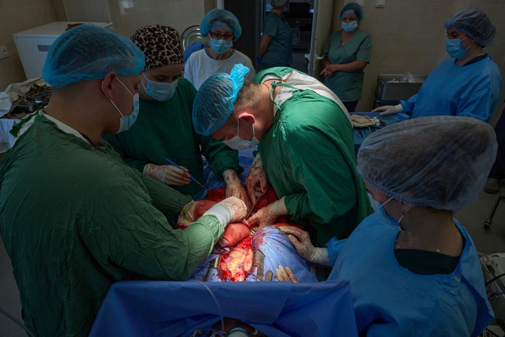 A wider perspective highlights the collective effort required during the extraction phase. Surrounded by surgical nurses and assisting staff who monitor every parameter, the lead surgeons work in absolute synchronization. In a wartime medical environment where resources must be managed with extreme efficiency, the seamless coordination of this team ensures that no movement is wasted and the donor's gift is preserved perfectly. (Photo: Mykyta Shandyba / UNITED24 Media) A group of Ukrainian surgeons and surgical nurses collaborating over an open chest cavity during an organ procurement operation in Kyiv.