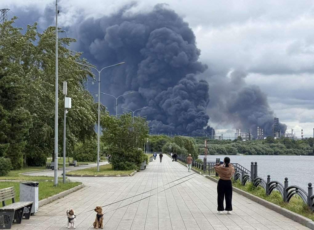 People walk in a park as black smoke rises from the area of the Russian oil producer Gazprom Neft's Moscow oil refinery on the south-eastern outskirts of Moscow on June 18, 2026. (Photo by AFP via Getty Images)