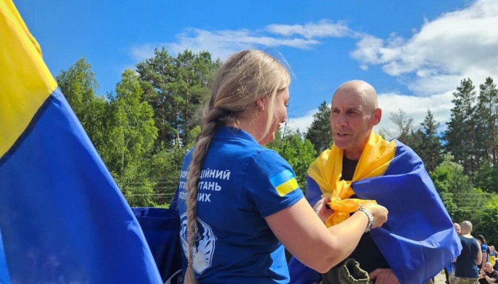 Ukrainian soldier with national flags draped over their shoulders after returning home in Ukraine, on June 26, 2026. (Source: Coordination Headquarters for the Treatment of Prisoners of War)