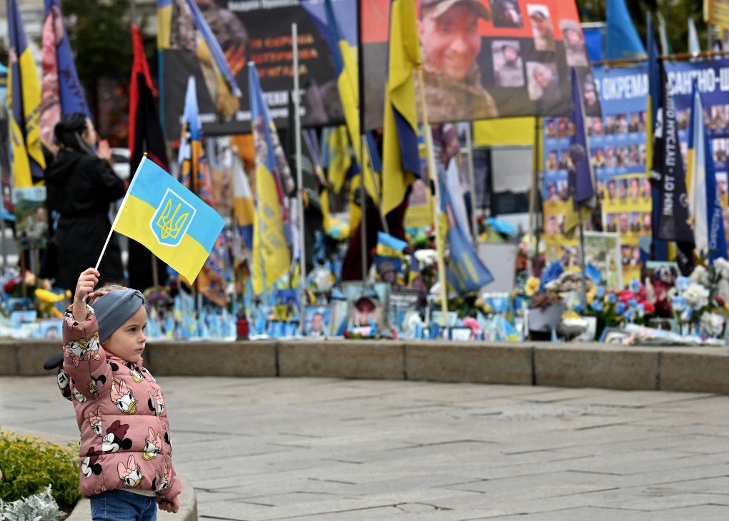 A girl holds a Ukrainian flag at a makeshift memorial for fallen Ukrainian and foreign soldiers on Independence Square in Kyiv on October 4, 2025, amid the Russian invasion in Ukraine. Photo: SERGEI SUPINSKY/AFP via Getty Images