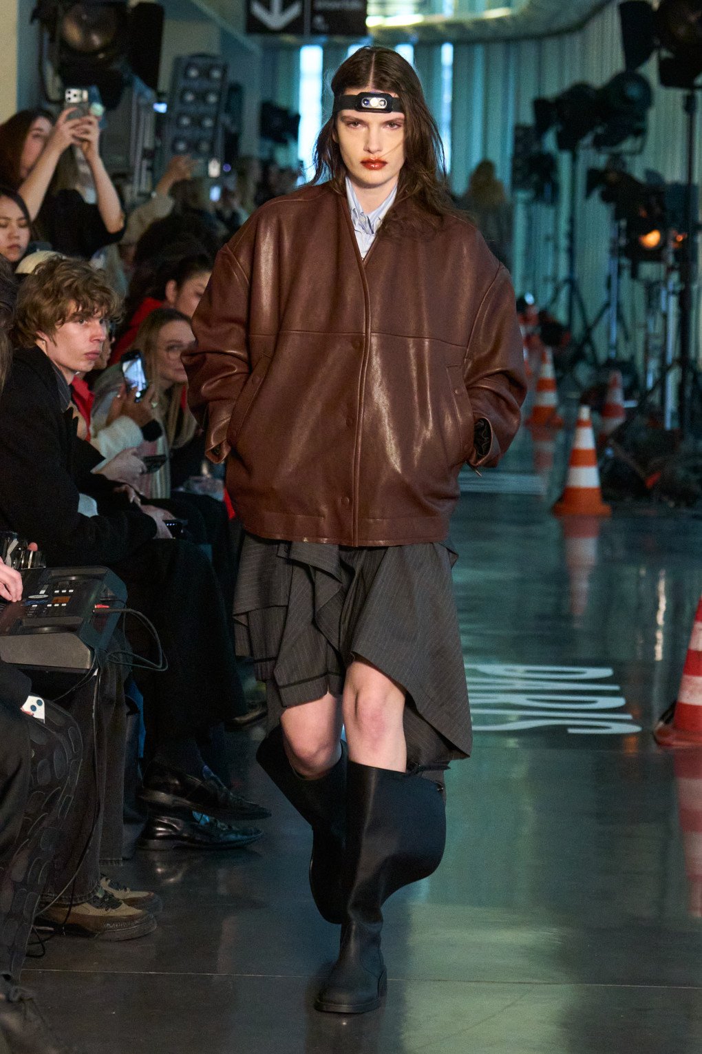 A model in a oversized brown leather jacket layered over a dark skirt walks down the runway with confidence. (Source: LITKOVSKA press office)