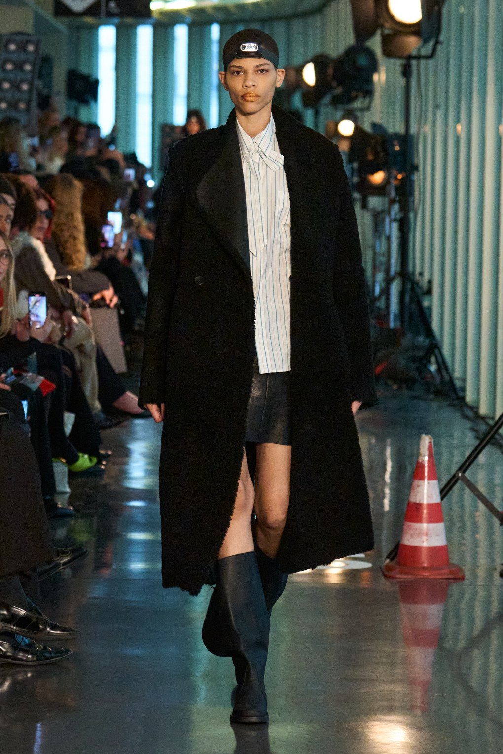 A model walks with confidence in a mix of classic and avant-garde, wearing a black coat paired with a striped shirt and a headlamp. (Source: LITKOVSKA press office)
