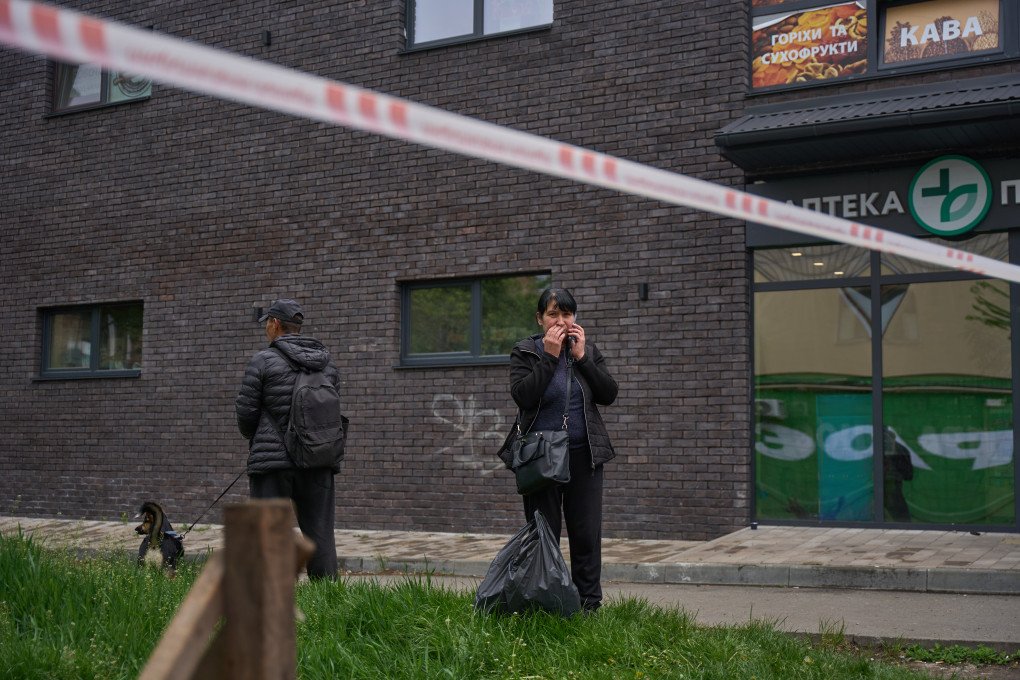 Un hombre con su perro y una mujer permanecen detrás de la cinta policial frente a una farmacia dañada en Kyiv el 7 de mayo de 2025, horas después de que un ataque ruso con drones y misiles sacudiera la ciudad.