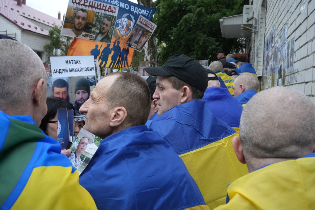 Former prisoners of war, draped in Ukrainian flags, gather outside the exchange site on June 19. Photo: Josh Olley for UNITED24 Media