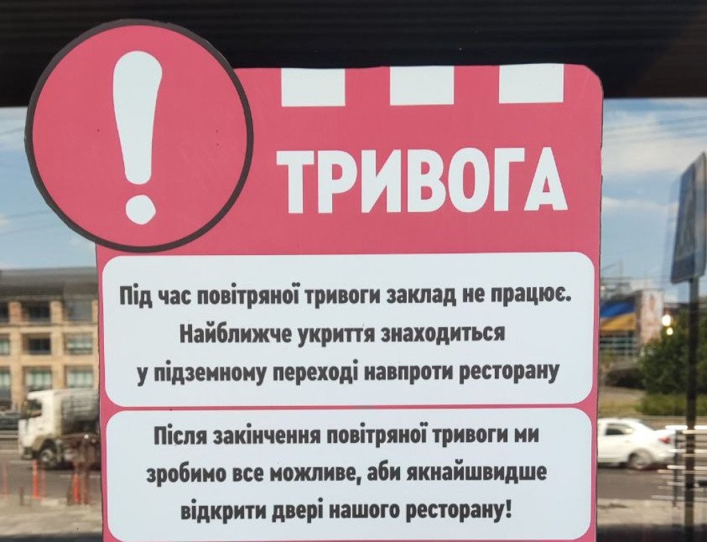 Un cartel en la puerta de KFC dice: “Durante una alerta antiaérea, el restaurante permanece cerrado. El refugio más cercano se encuentra en el pasaje subterráneo frente al restaurante. Una vez finalizada la alerta, haremos todo lo posible por reabrir nuestro restaurante cuanto antes”. Julio de 2025, Kiev. Foto: United24 Media. Un cartel en la puerta de KFC dice: “Durante una alerta antiaérea, el restaurante permanece cerrado. El refugio más cercano se encuentra en el pasaje subterráneo frente al restaurante. Una vez finalizada la alerta, haremos todo lo posible por reabrir nuestro restaurante cuanto antes”. Julio de 2025, Kiev. Foto: United24 Media.