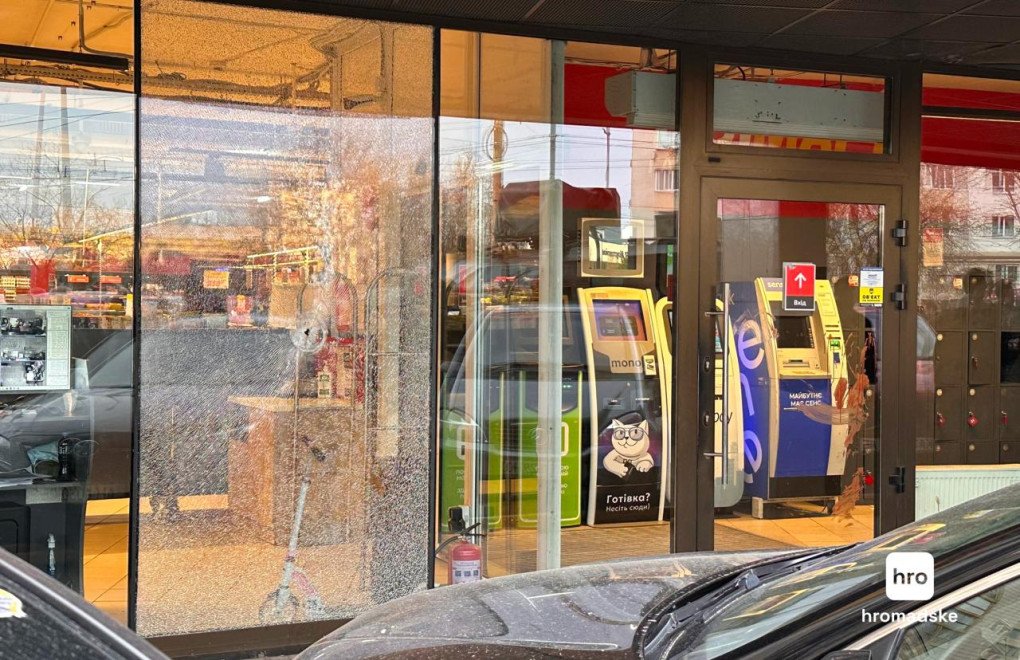 A bullet hole pierces the shattered glass facade of the supermarket, revealing an abandoned child’s scooter inside. (Source: Hromadske)