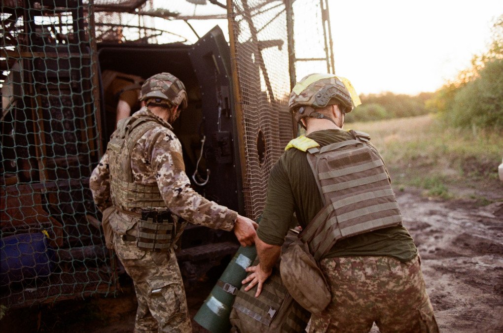 A soldier hands another a backpack and mat as they come off positions. Ukraine, August 2025. Photo by Lucile Brizard/UNITED24 Media.
