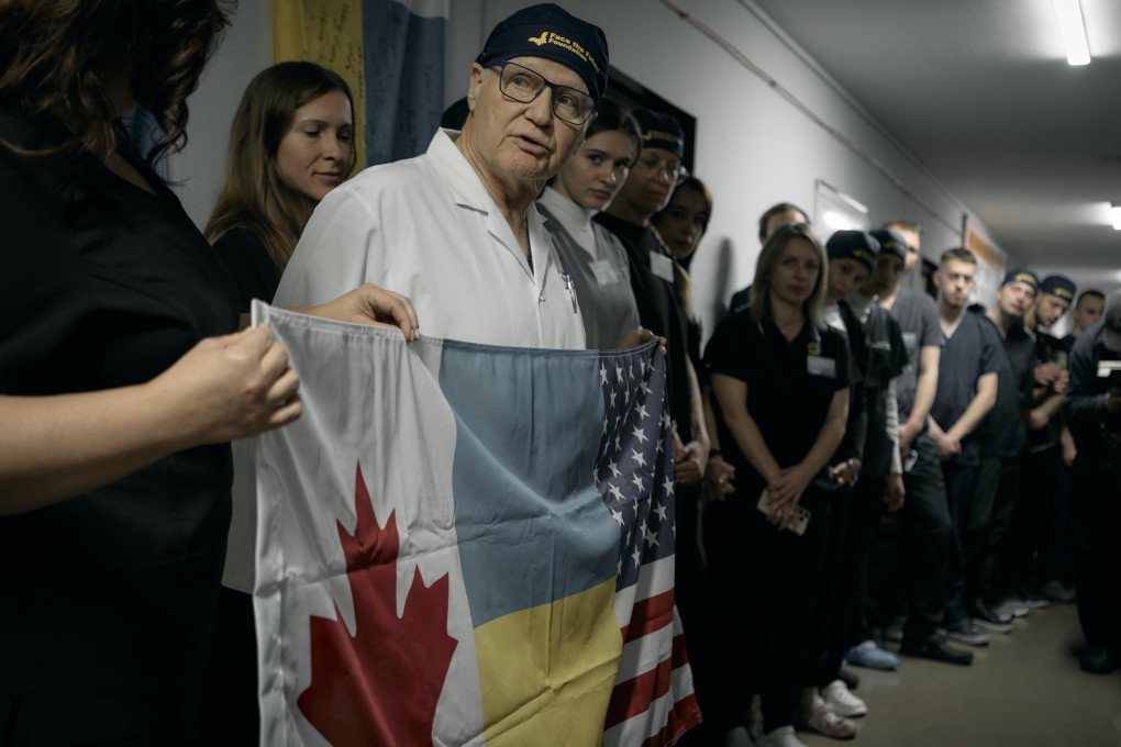 Un equipo de médicos canadienses, estadounidenses y ucranianos se reúne antes del inicio de las cirugías, en lo que será la sexta Misión "Enfrentando el Futuro". Llevan una bandera en sus manos, que será firmada por los pacientes y el personal. Foto: Josh Olley/ UNITED24 Media