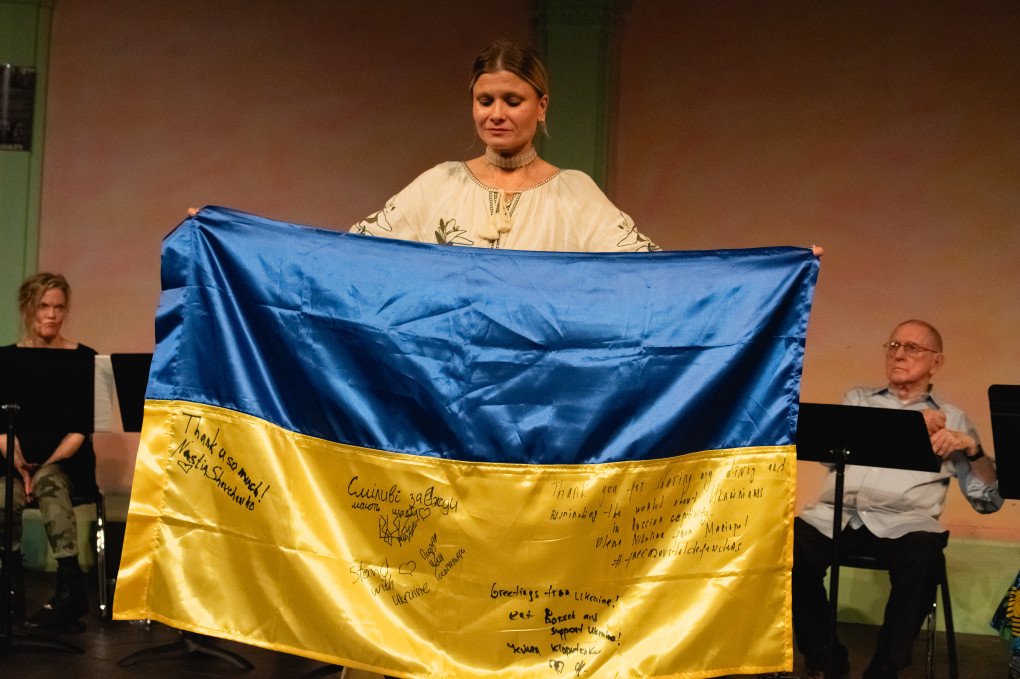 Daria Kolomiec at the June 2, 2024, “Diary of War” reading, standing with the Ukrainian flag bearing the inscription “Happiness favors the brave” — written by Iryna “Cheka” Tsybukh, who signed the flag just weeks before her death. Photo: Anastasia Krasheninnikova Daria Kolomiec at the June 2, 2024, “Diary of War” reading, standing with the Ukrainian flag bearing the inscription “Happiness favors the brave” — written by Iryna “Cheka” Tsybukh, who signed the flag just weeks before her death. Photo: Anastasia Krasheninnikova