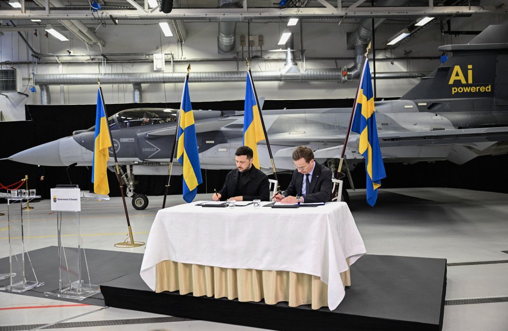 Swedish Prime Minister Ulf Kristersson (R) and Ukrainian President Volodymyr Zelensky sign documents during a joint press conference in front of a Gripen fighter jet in Linkoping, Sweden, on October 22, 2025. (Photo by Fredrik Sandberg via Getty Images)