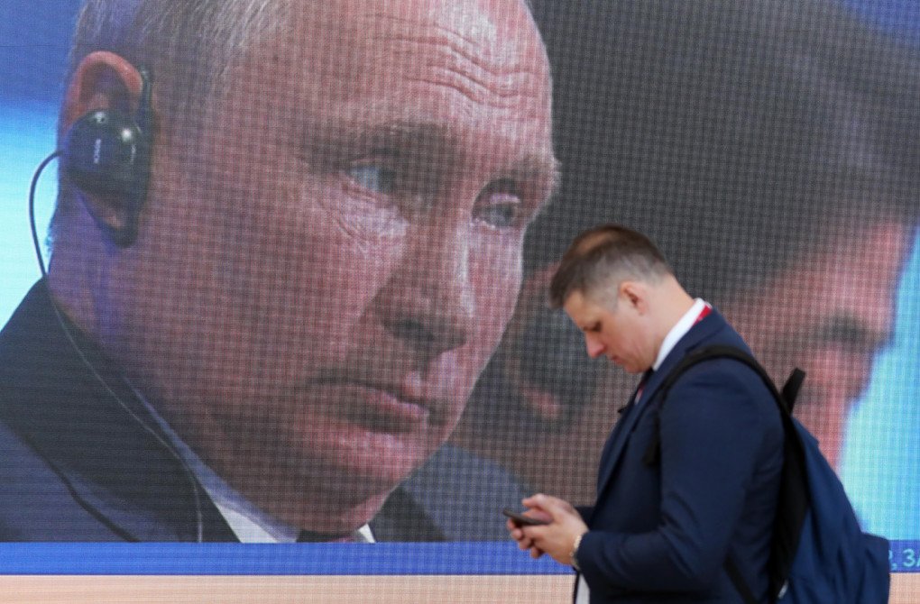 An attendee checks his smartphone as he walks past a screen showing Russia’s leader, Vladimir Putin (Source: Chris Ratcliffe via Getty Images)