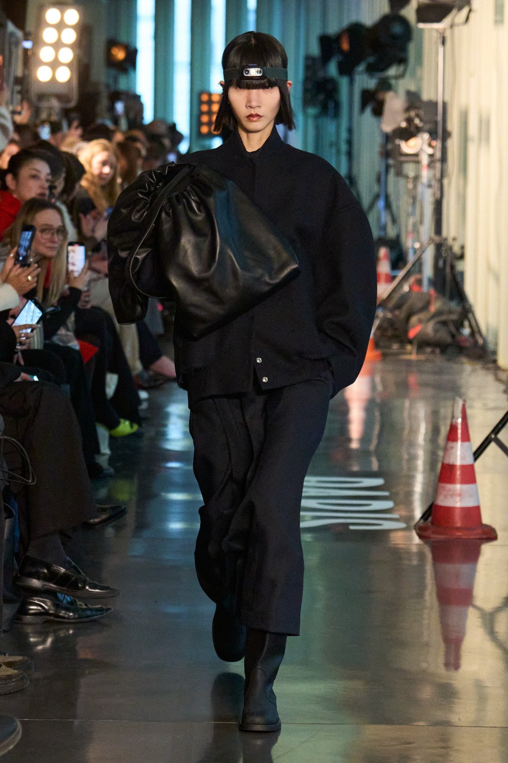 A model struts the runway in an oversized black ensemble, featuring a boxy jacket, wide pants, and a sleek headlamp. (Source: LITKOVSKA press office)