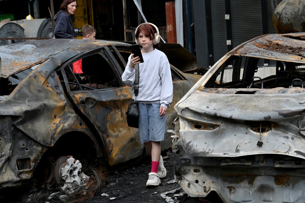 A girl listens to music as she walks past burned out vehicles parked outside a shopping mall following a night-time drone attack on Kyiv, on May 4, 2025 amid the Russian invasion of Ukraine. Photo: SERGEI SUPINSKY/AFP via Getty Images