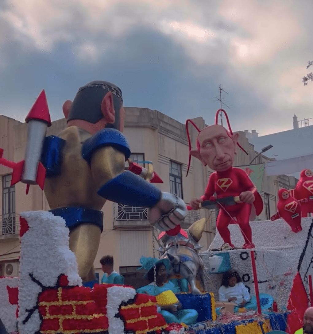 A close-up of the carnival float showing a larger-than-life Putin figure in a superhero costume, holding rockets and surrounded by red-suited figures, at the Entrudo Carnival in Portugal. (Source: Alona Kuznetsova/Threads)