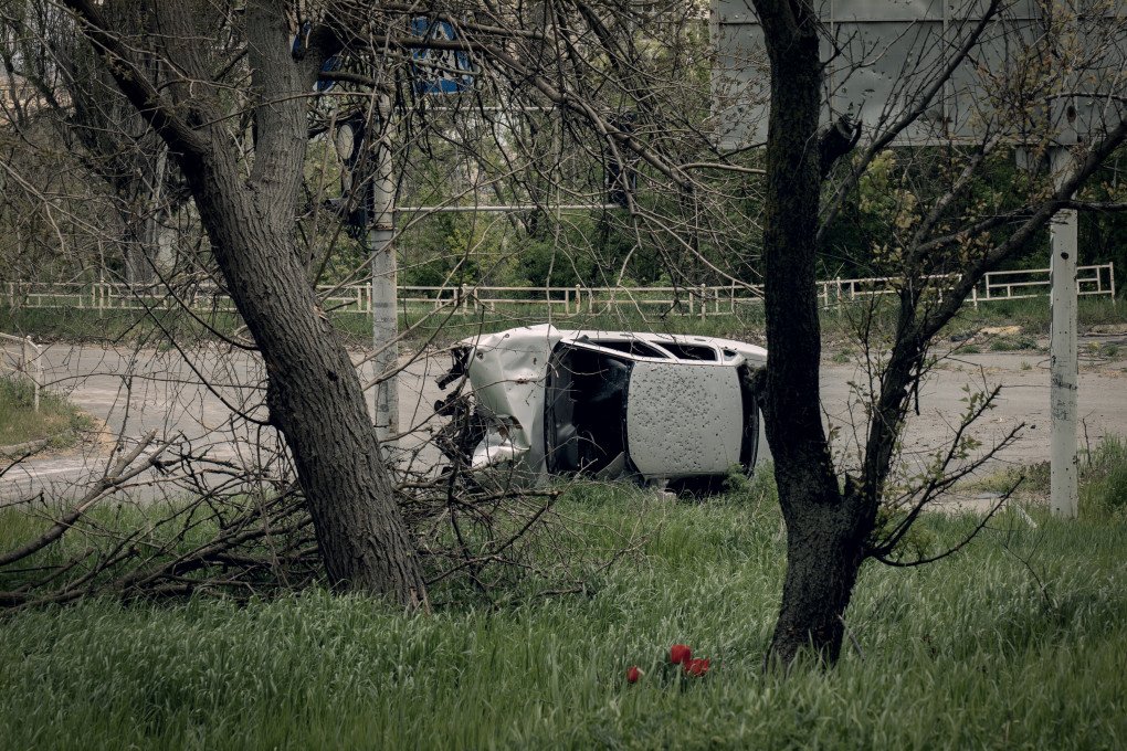 A destroyed car sits behind freshly bloomed flowers along the banks of the Dnipro River. Kherson, Ukraine, May 2026. Photo: Joshua Olley / UNITED24 Media.