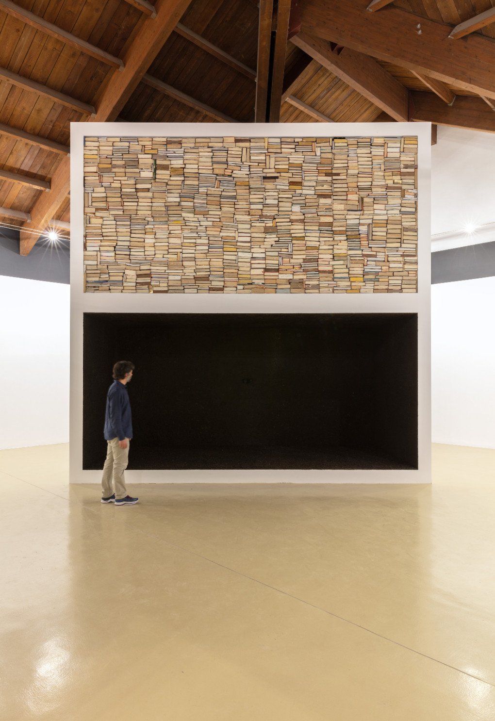 In Shelter II, the upper level contains books suggesting how to protect homes from shattered glass during bombings, while the lower level, marked by dirt-covered walls, evokes the claustrophobic experience of living in a shelter as if buried alive. (Source: nikitakadan.com)
