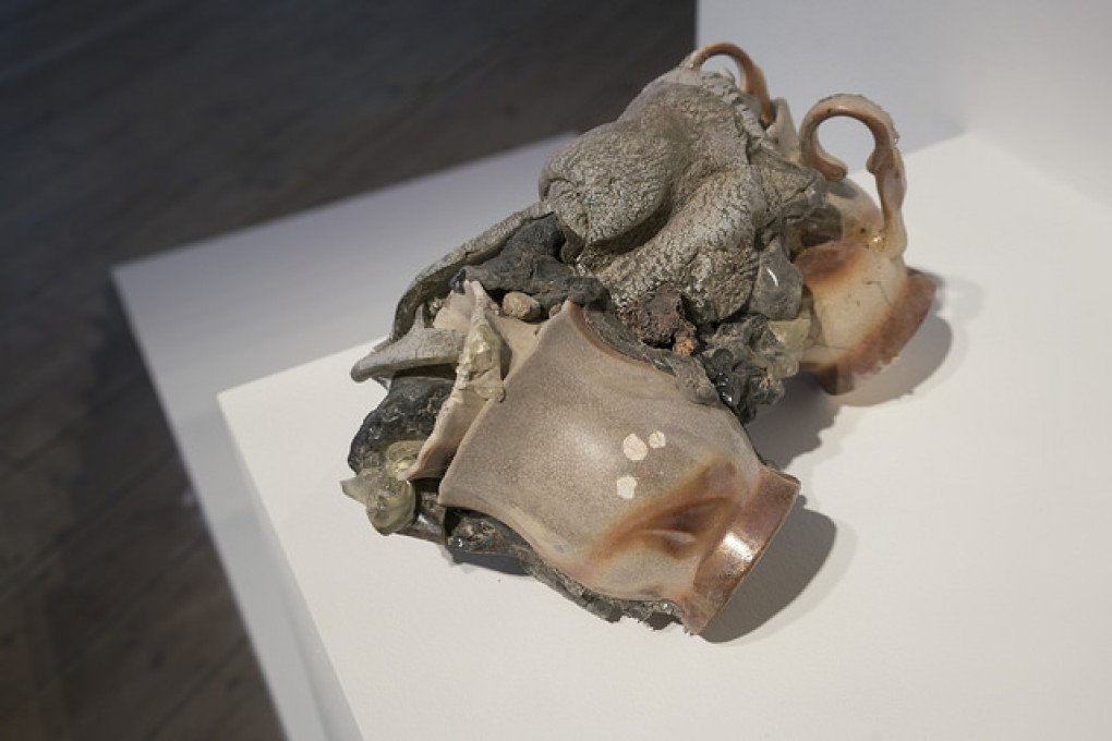 Victory (White Shelf) by Kadan is a reinterpretation of Vasyl Ermilov’s 1925 model of the Monument to Three Russian Revolutions. The original hammer-shaped form is rendered in white plywood and stripped of its communist symbolism. On top, a small assemblage of melted cups—found in the remains of a house in Ukraine’s Lysychansk destroyed by artillery shelling—rests on the structure. (Source: nikitakadan.com)