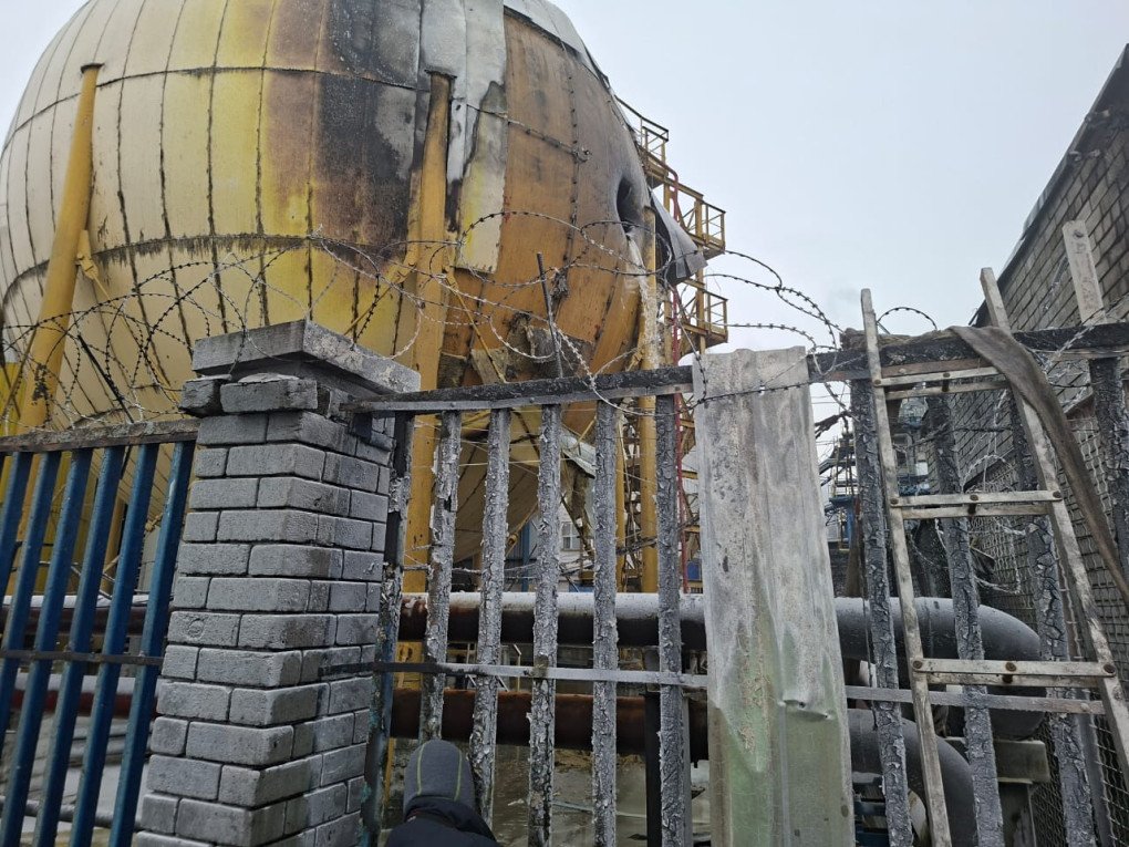 A close-up view through the fence showing the burn marks and damage to one of the facility’s spherical storage tanks. (Source: State Emergency Service)