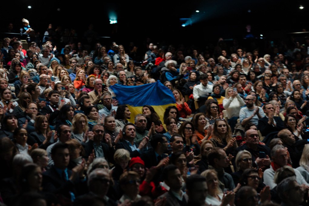 The audience at Théâtre de la Ville–Sarah Bernhardt rises in applause, with a Ukrainian flag visible among spectators during the opening night of Le Voyage en Ukraine. (Source: Mykola Kolisnyk / Ukrainian Institute in France)