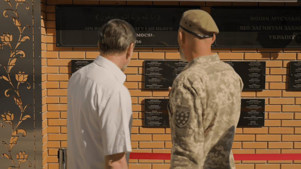 People stand before the memorial, reading the names engraved on its walls. Photo: UNITED24 Media 